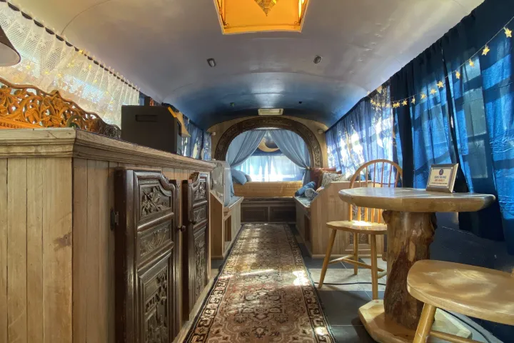 Cozy bus interior with wood cabinets, rug, table, chairs, and blue curtains.