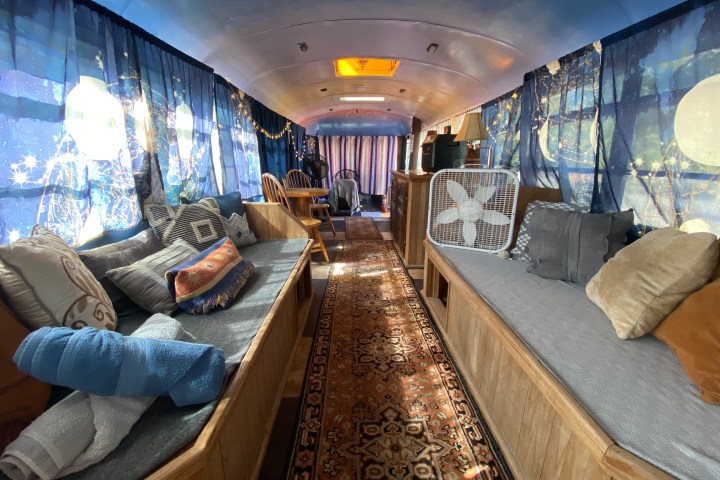 Interior of a cozy bus with couches, pillows, and patterned curtains.
