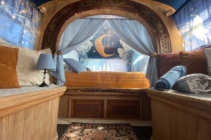 Cozy bed nook with celestial decor, draped curtains, and pillows, featuring a crescent moon wall art.